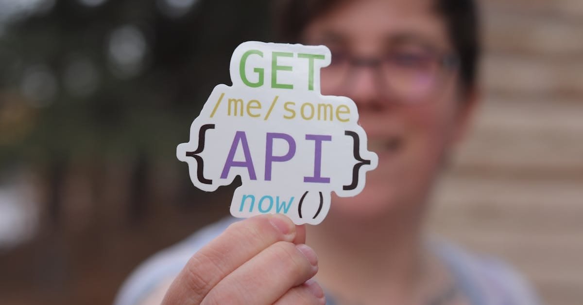Close-up of a person holding a colorful API-themed sticker with trees blurred in the background.
