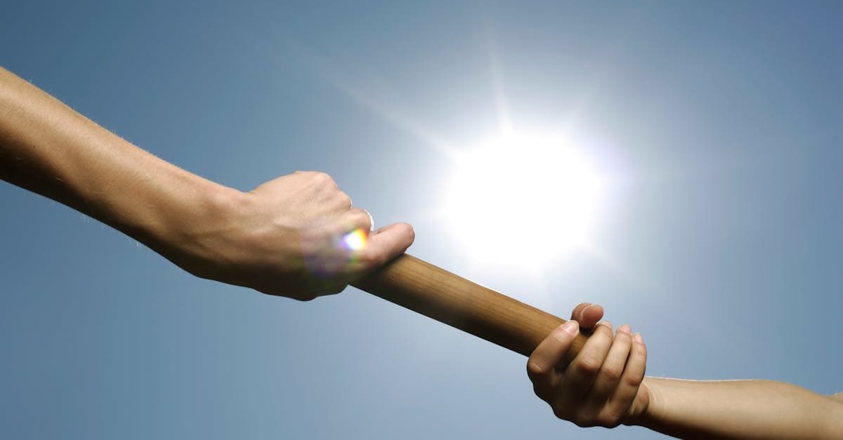 Close-up of hands passing a relay baton against a bright sunny sky.
