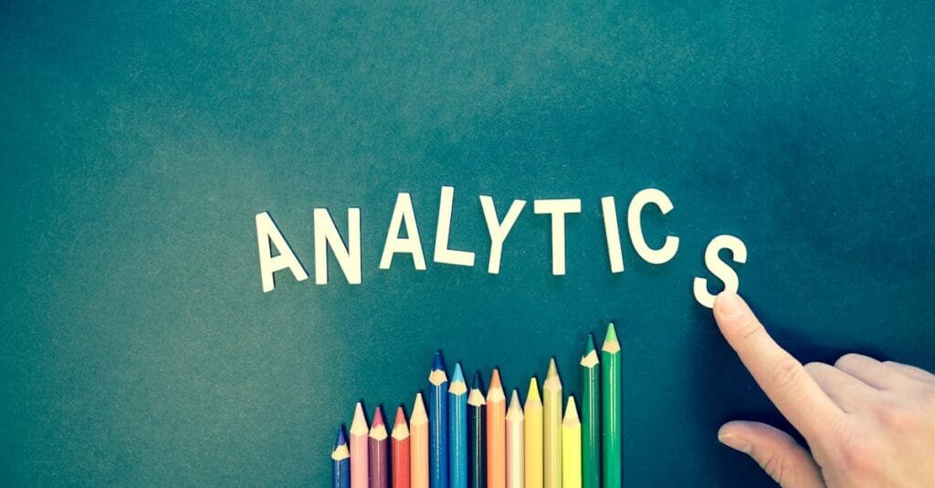 Colored pencils and letters spelling 'ANALYTICS' on a textured background with a hand.