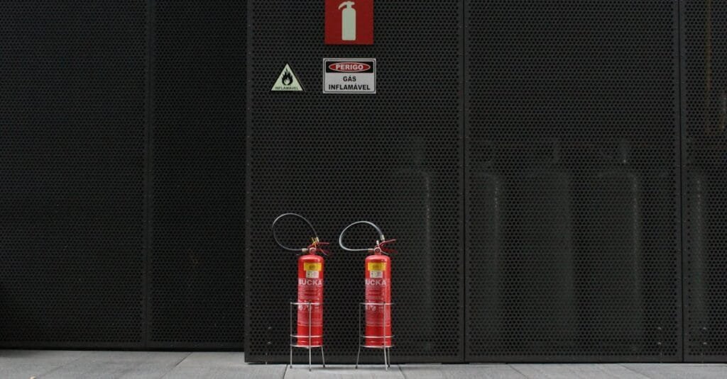 Red fire extinguishers against industrial metal wall with warning signs.