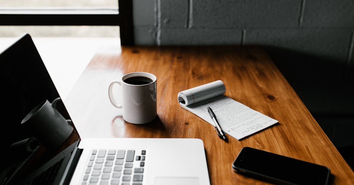 A tidy workspace featuring a laptop, coffee cup, phone, and notepad on a wooden desk.