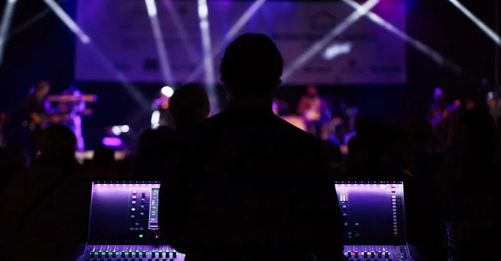 A sound engineer manages the audio mixer during a vibrant live concert with colorful lighting.