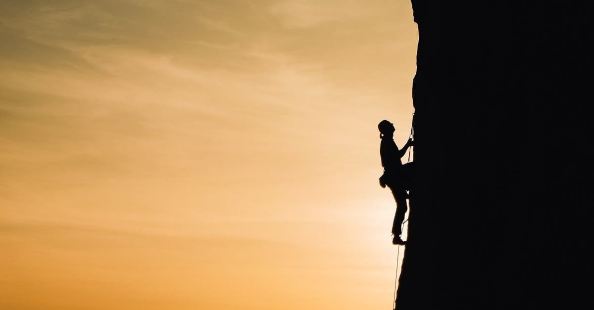 A silhouette of a rock climber scaling a steep cliff during sunset in Russia, showcasing determination and adventure.