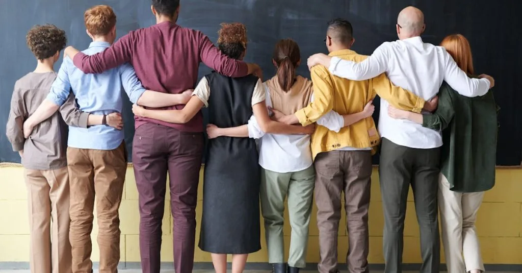 A diverse group of adults in casual outfits hugging in front of a chalkboard, symbolizing teamwork.