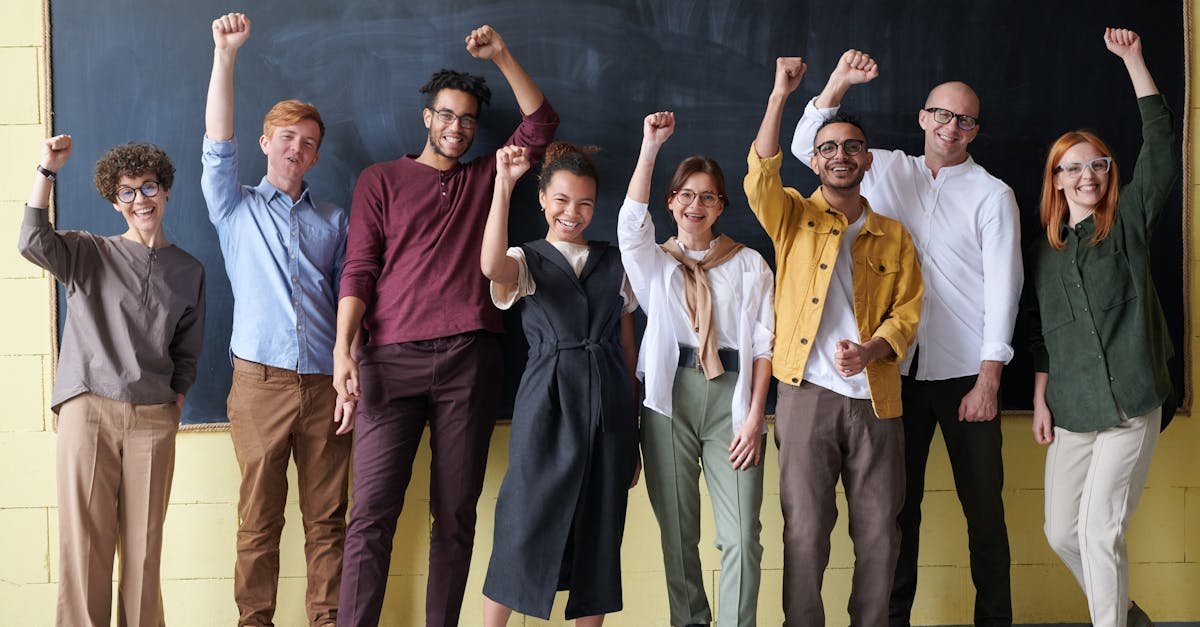 A group of eight adults cheerfully standing with raised fists in front of a blackboard indoors.