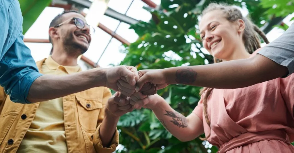 A group of young adults celebrating teamwork with a fist bump in a lush outdoor setting.