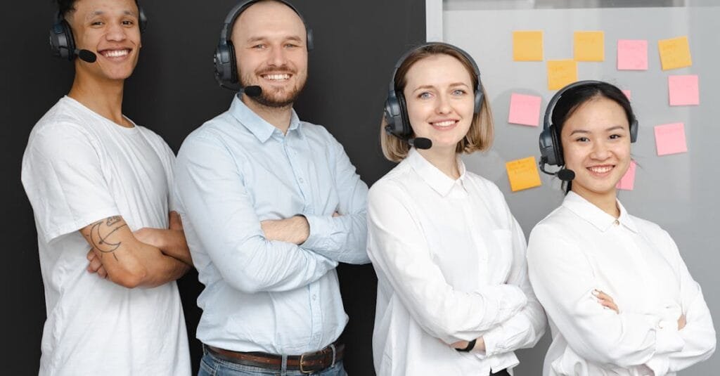 Team of diverse call center professionals smiling and standing confidently with headsets and microphones.