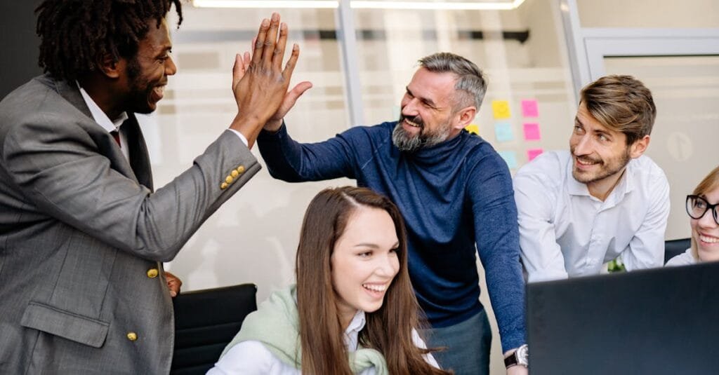 A diverse team happily celebrates a workplace achievement with high-fives.