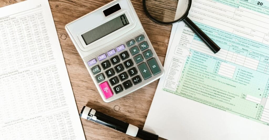 Top view of tax forms, a calculator, and a magnifying glass on a wooden surface, ideal for accounting themes.