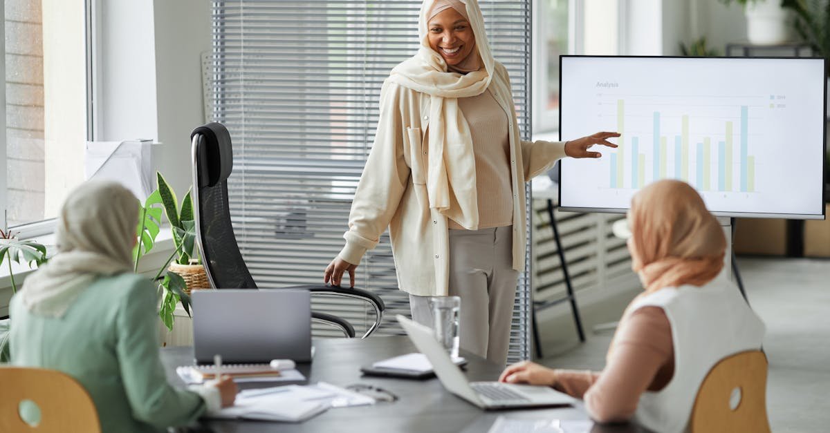 A diverse group of businesswomen in hijabs discussing data in a modern office setting.