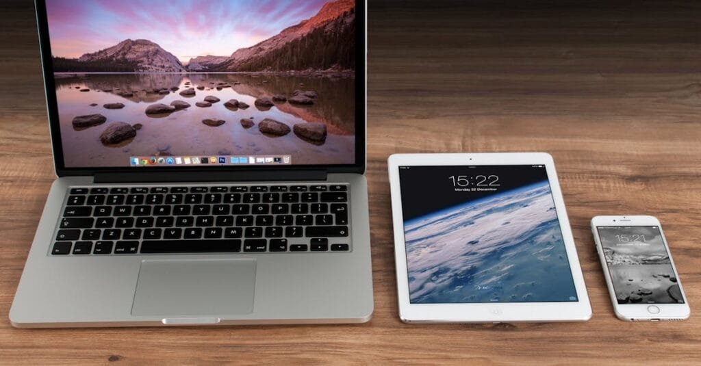 Modern workspace showcasing Apple laptop, tablet, and smartphone on a wooden desk.