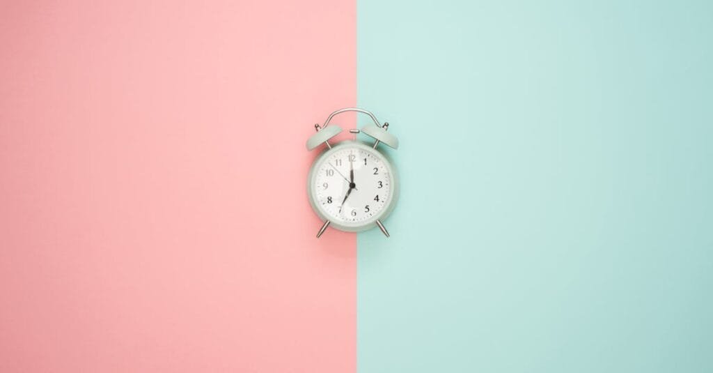 A vintage round clock on a split pastel pink and blue background.