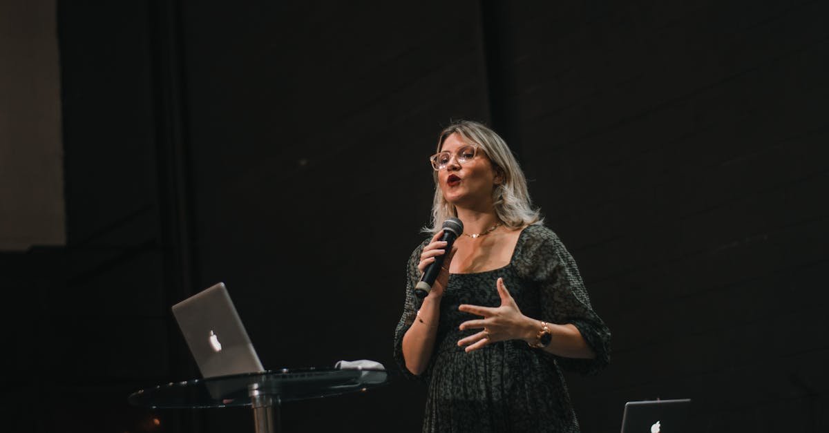 A confident woman delivers a speech on stage with a microphone and laptop.