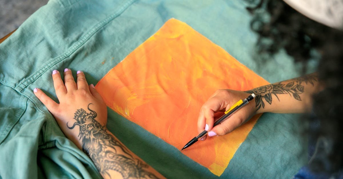Tattooed artist adds bright orange artwork to a green jacket, showcasing creativity and design.