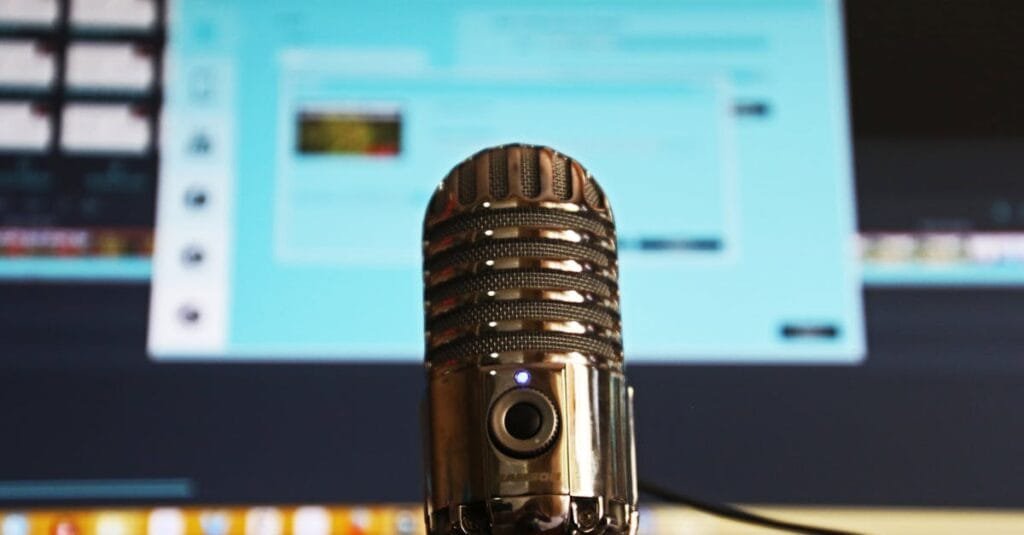 Close-up of a microphone with a blurred computer screen in the background, ideal for podcast themes.