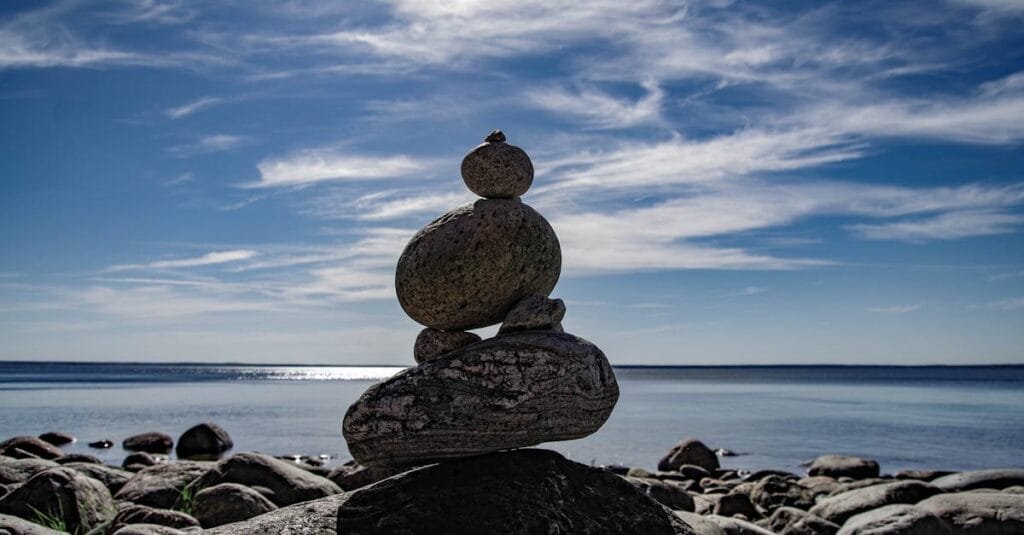 A tranquil scene of balanced rocks by the ocean under a clear blue sky.