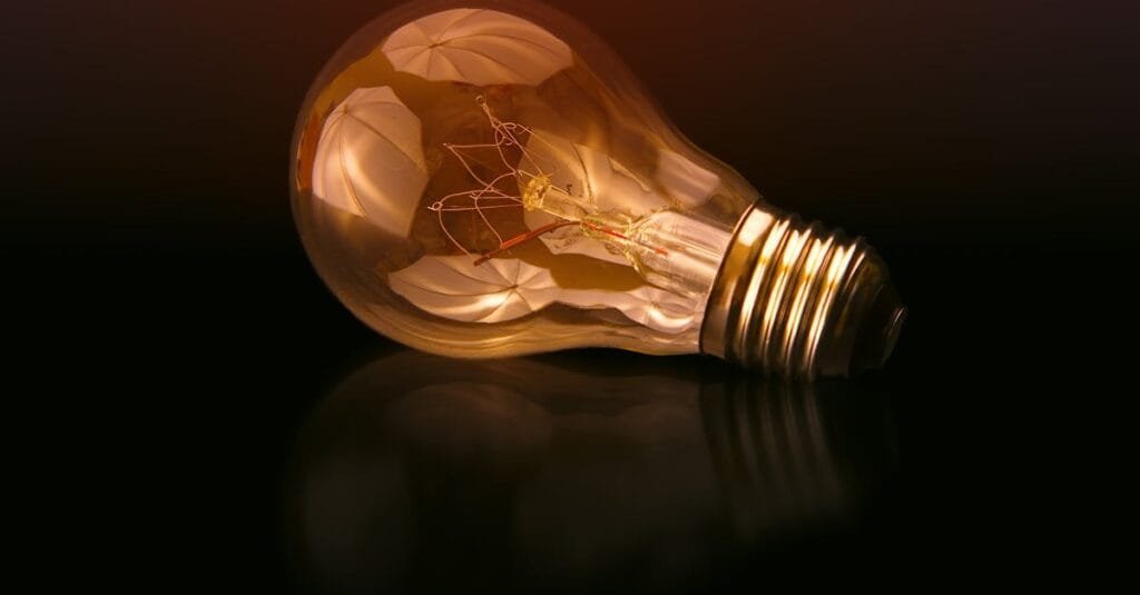 A detailed close-up of a light bulb showcasing its intricate filament and glowing glass against a dark reflective surface.