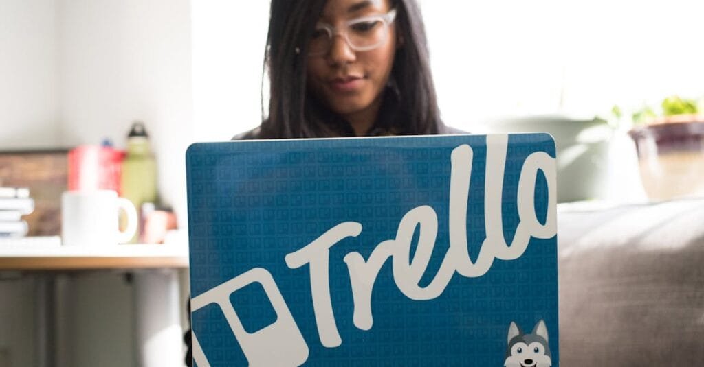Focused woman engaged in remote work using a Trello-branded laptop in a cozy indoor setting.