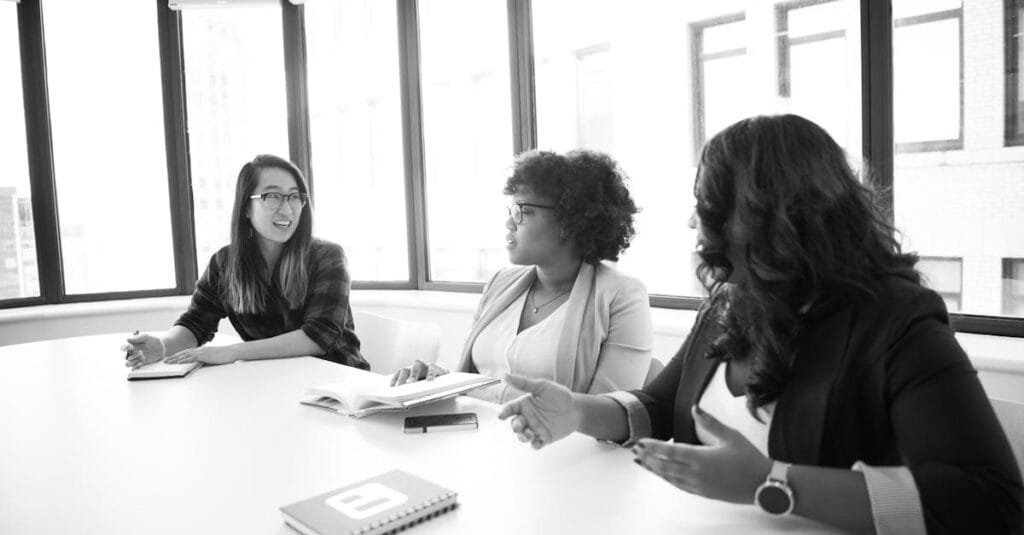 Three women engaged in a business meeting around a table in a modern office setting.