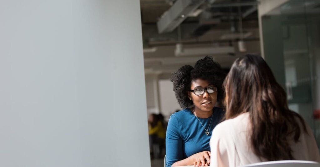 Two women engaged in a discussion in a modern office environment, highlighting communication and interaction.