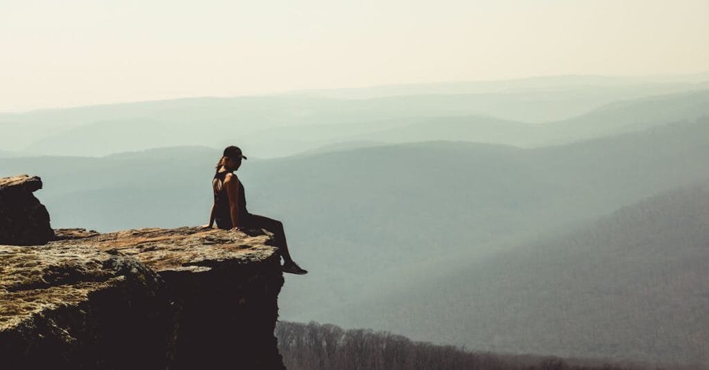 Woman sitting on a cliff edge overlooking a vast mountain landscape in Arkansas.