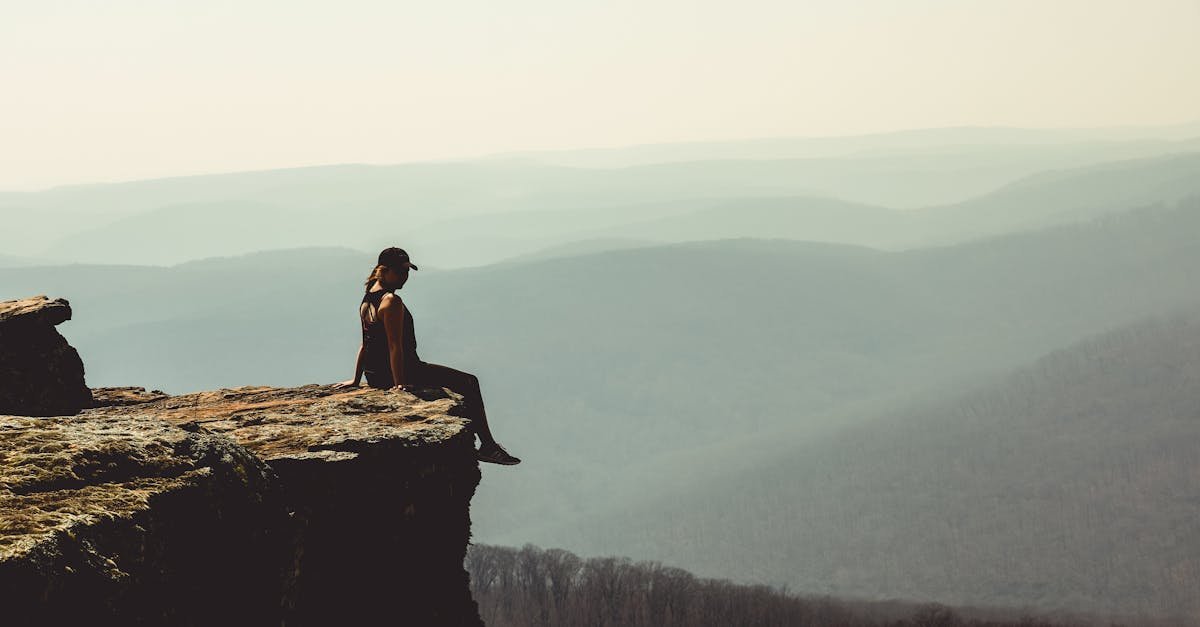 Woman sitting on a cliff edge overlooking a vast mountain landscape in Arkansas.