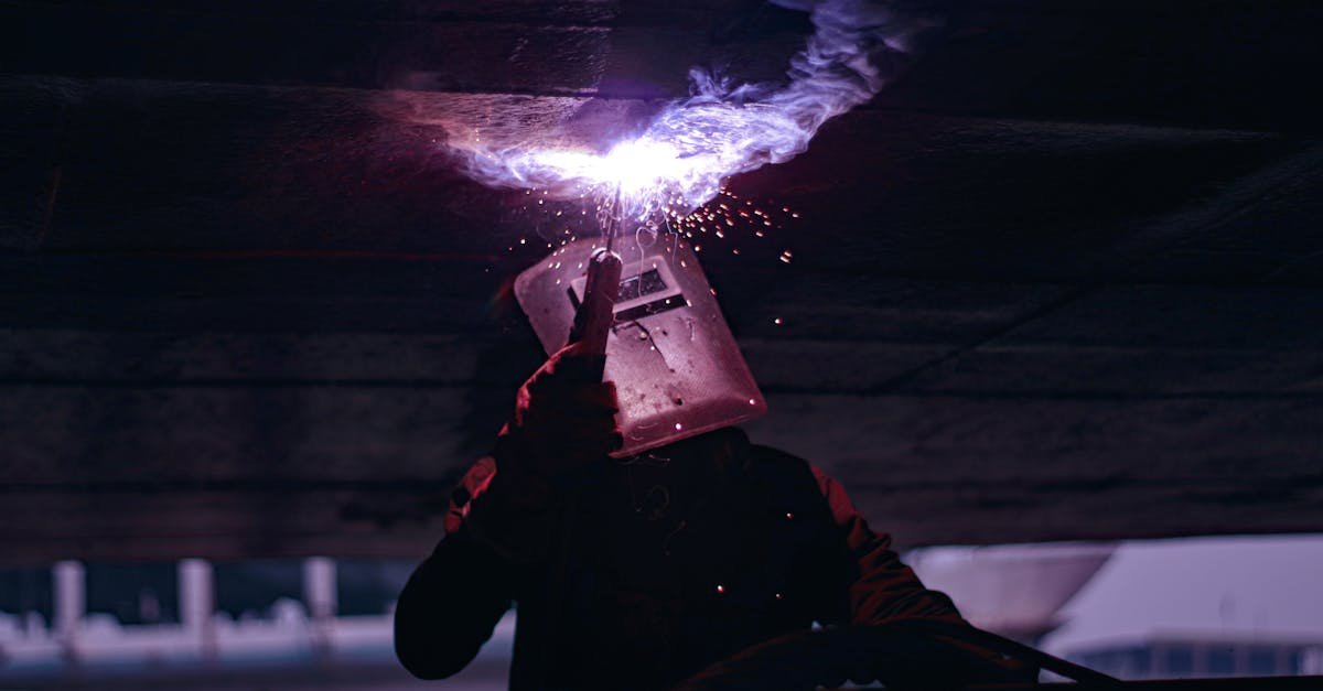 Silhouetted welder working under large metal structure, sparks flying, industrial setting.