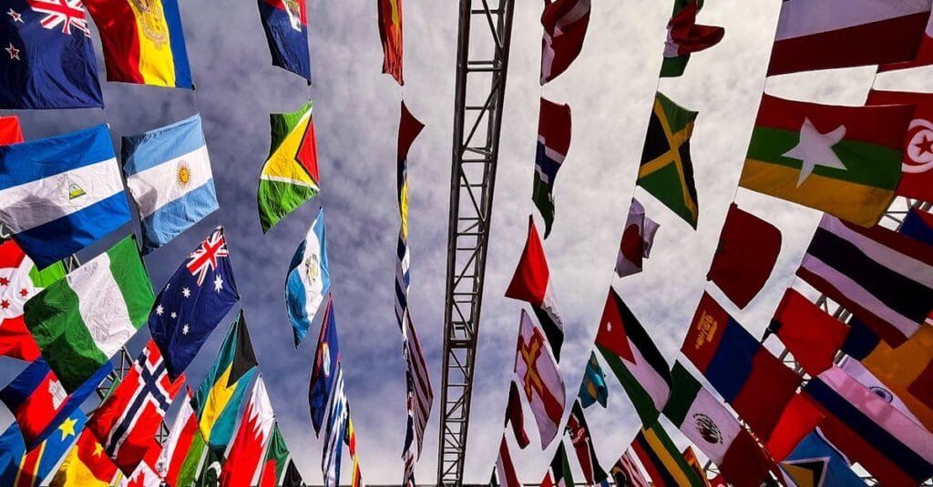 A dynamic low angle shot of various international flags hanging outdoors against a cloudy sky.