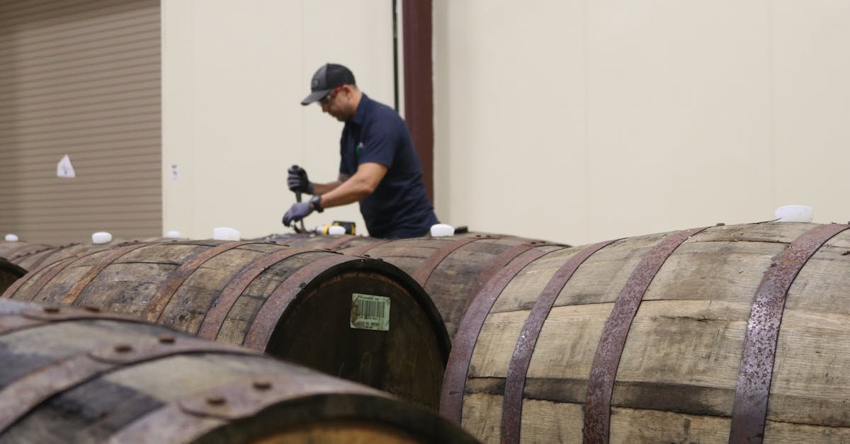 A worker carefully inspecting wooden barrels in a winery room, ensuring quality.