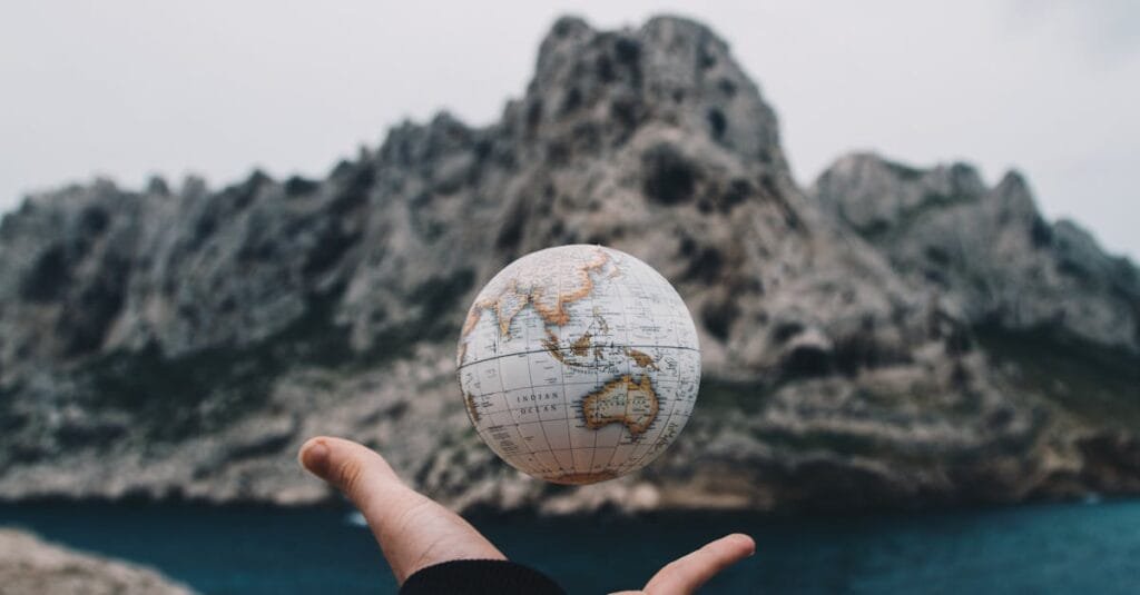 A hand holding a floating globe with a scenic Marseille backdrop, capturing adventure and exploration.
