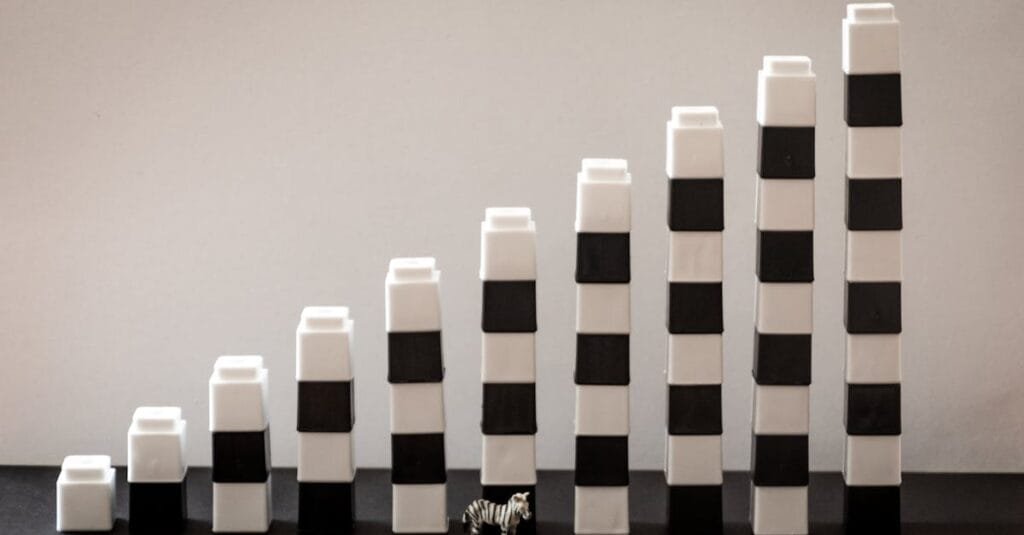Black and white blocks steadily stacked, forming a gradual rise with a tiny zebra figurine in front.