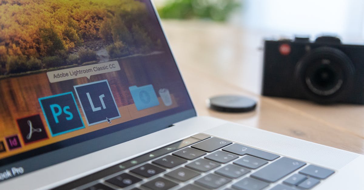 Close-up of a laptop displaying Adobe software icons, beside a camera on a desk.