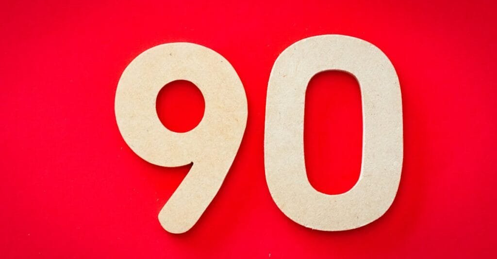 Minimalist depiction of wooden numbers '90' against a vivid red backdrop, capturing simplicity and elegance.