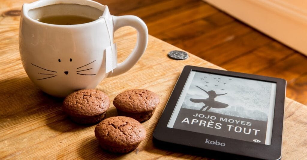 A cozy scene with tea, muffins, and an e-reader on a wooden table.