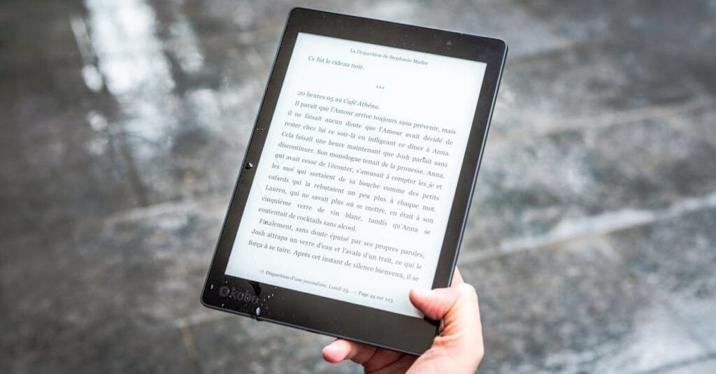 A person holds an e-reader displaying text against a wet pavement background.