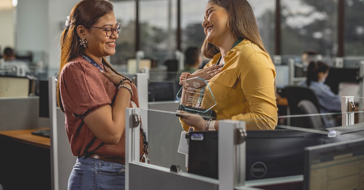 Two women smile and share a joyful moment receiving an award in a modern office setting.