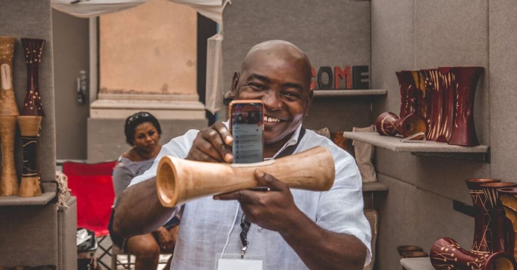 A cheerful artisan showcasing a handmade wooden piece at an indoor craft market.