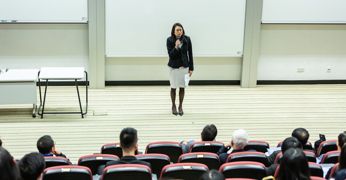 Female speaker presenting to an audience in a modern auditorium setting.