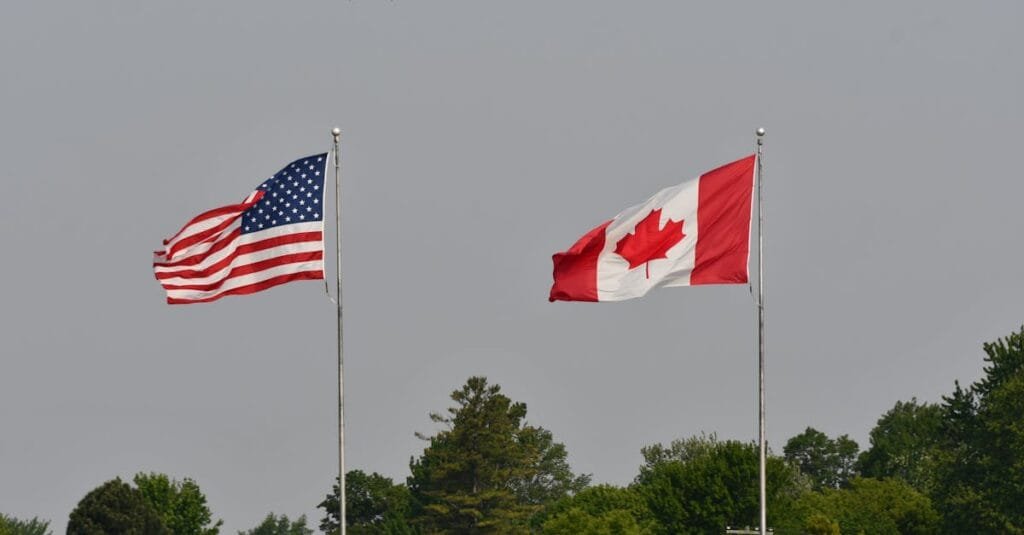 Flags of the USA and Canada waving on flagpoles against a clear sky in Sarnia, Ontario.