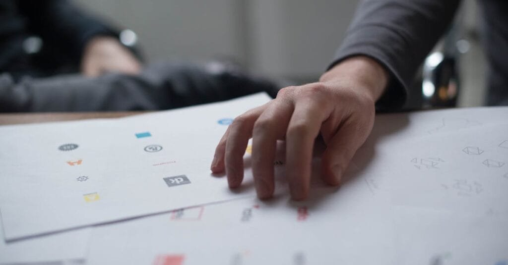 A close-up shot of a hand reviewing various logo designs on paper, ideal for business concepts.