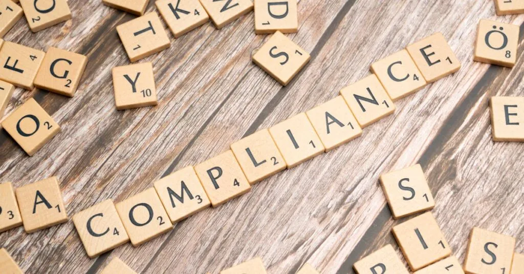 Wooden letter tiles forming the word 'COMPLIANCE' on a rustic wooden background.