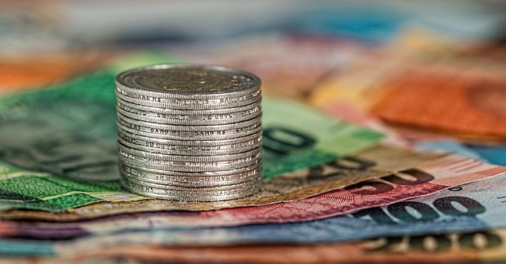 A stack of coins on top of various colored banknotes, symbolizing finance and currency.