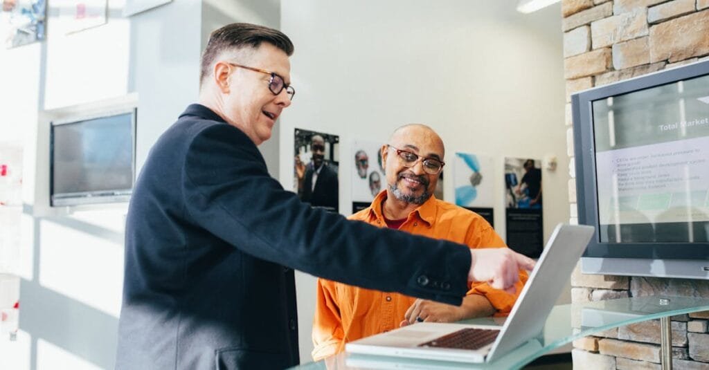 Two businessmen having a lively discussion in a modern office setting, pointing at a laptop screen.