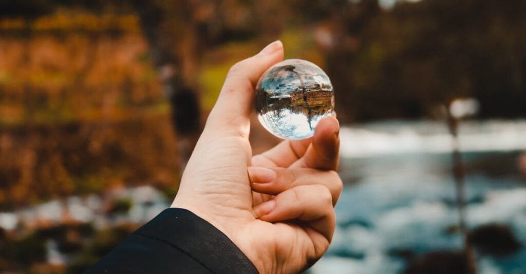 A hand holds a crystal ball, reflecting a vibrant autumn landscape.