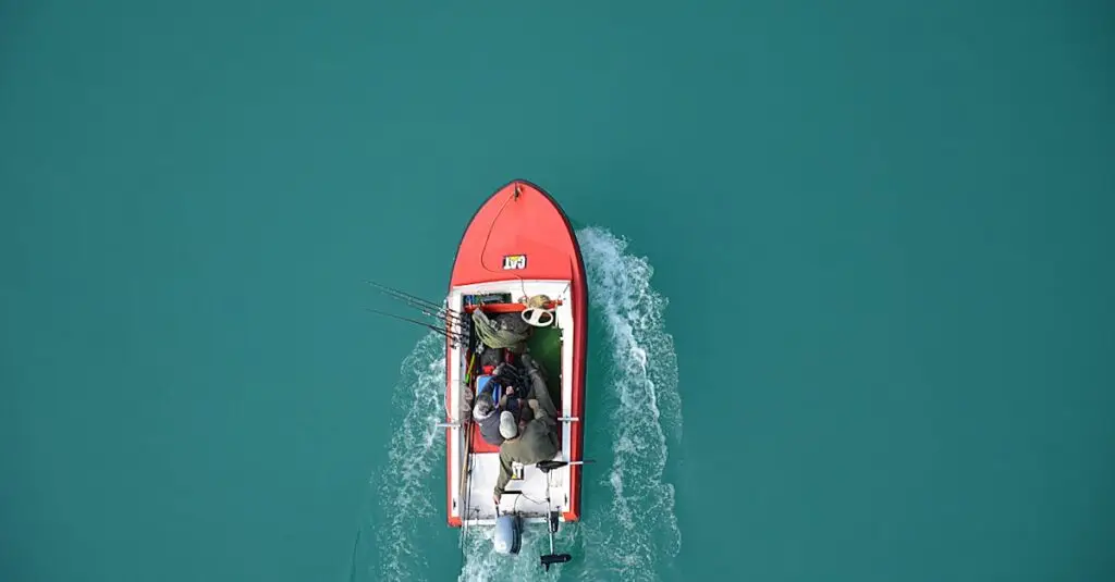 Top view of a red motorboat with fishermen navigating open turquoise waters.