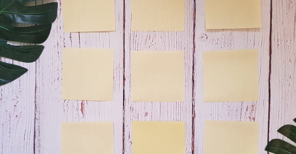 Flat lay of yellow sticky notes arranged on a rustic wooden surface with green leaves.
