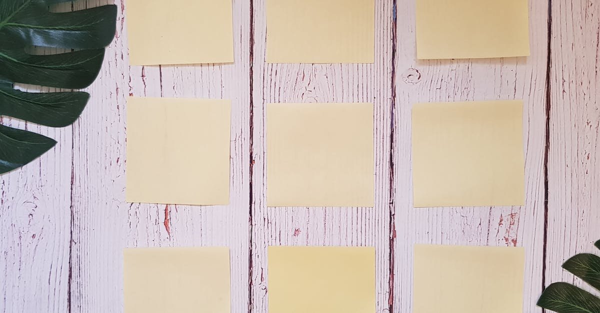 Flat lay of yellow sticky notes arranged on a rustic wooden surface with green leaves.