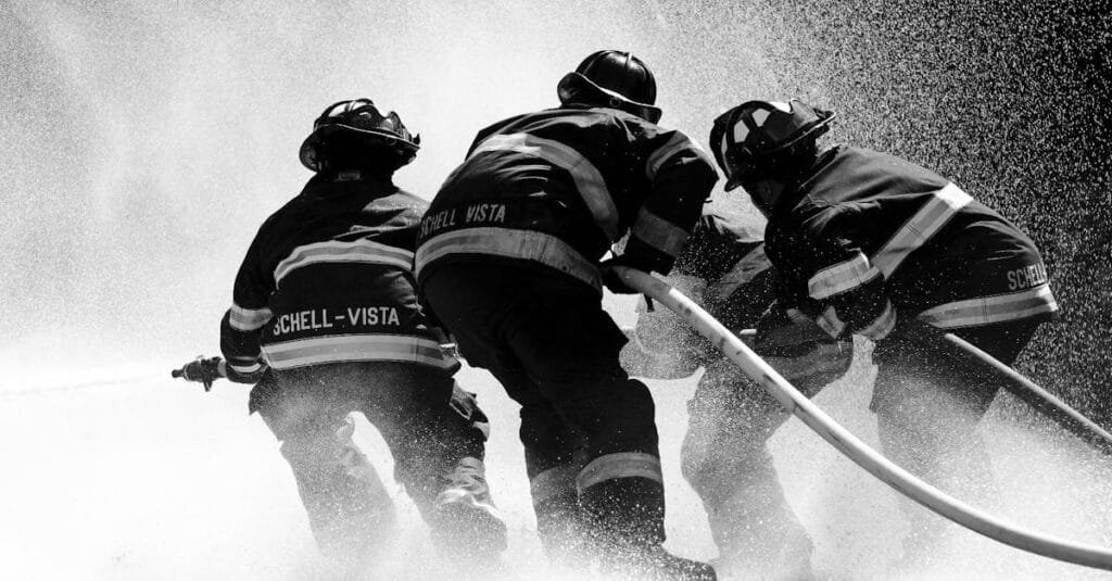 Firefighters in full gear battle heavy water spray in an intense operation.