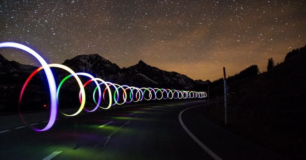 Enchanting long exposure of colorful light trails on a winding road beneath a star-filled sky.