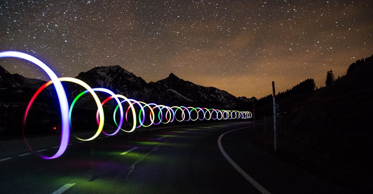 Enchanting long exposure of colorful light trails on a winding road beneath a star-filled sky.